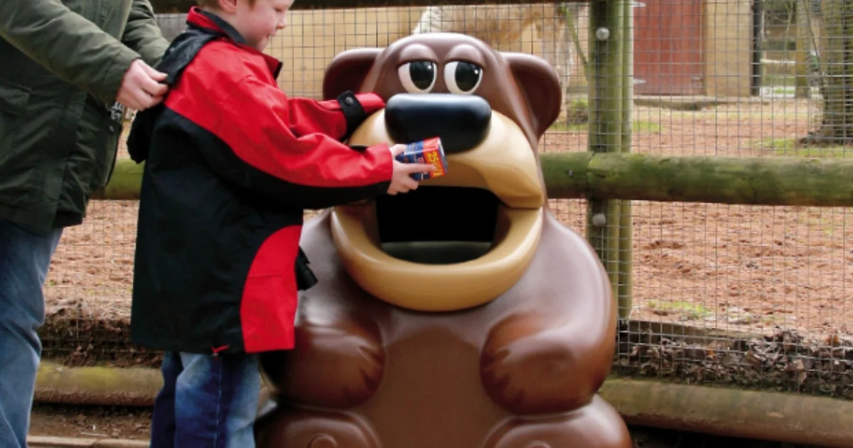 Young boy placing trash into a bear-shaped bin at a zoo